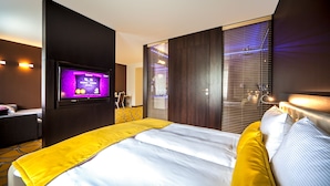 Una habitaci ón de hotel con cama, televisión, escritorio y ventana con persianas.