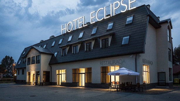 Un hotel llamado "Hotel Eclipse" con un diseño arquitectónico moderno, que cuenta con un letrero llamativo y un área de restaurante con mesas al aire libre.