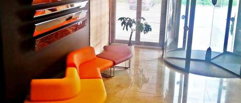 A reception area with a glass door, a potted plant, and orange seating.
