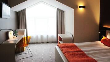 A hotel room with a bed, a desk, a chair, and a window with curtains.