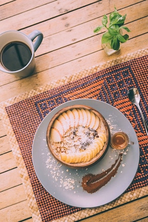 A dessert plate with sliced bananas, a small bowl of chocolate sauce, and a cup of coffee on a woven placemat. - The Birdhouse El Nido - Glamping (El Nido)