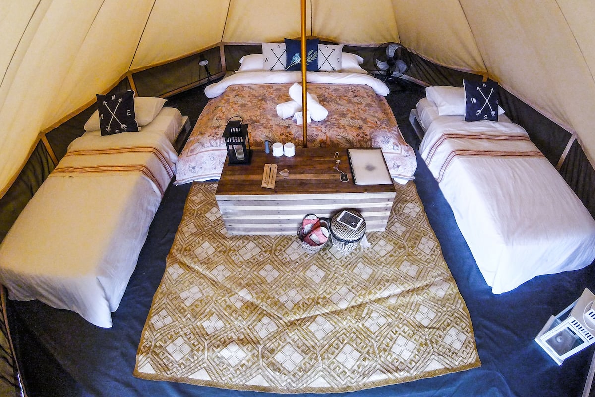 Una carpa con una cama, almohadas, una mesita y una manta.