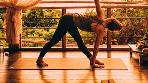 A person performing a yoga pose on a mat in a room with large windows and curtains. - The Birdhouse El Nido - Glamping (El Nido)