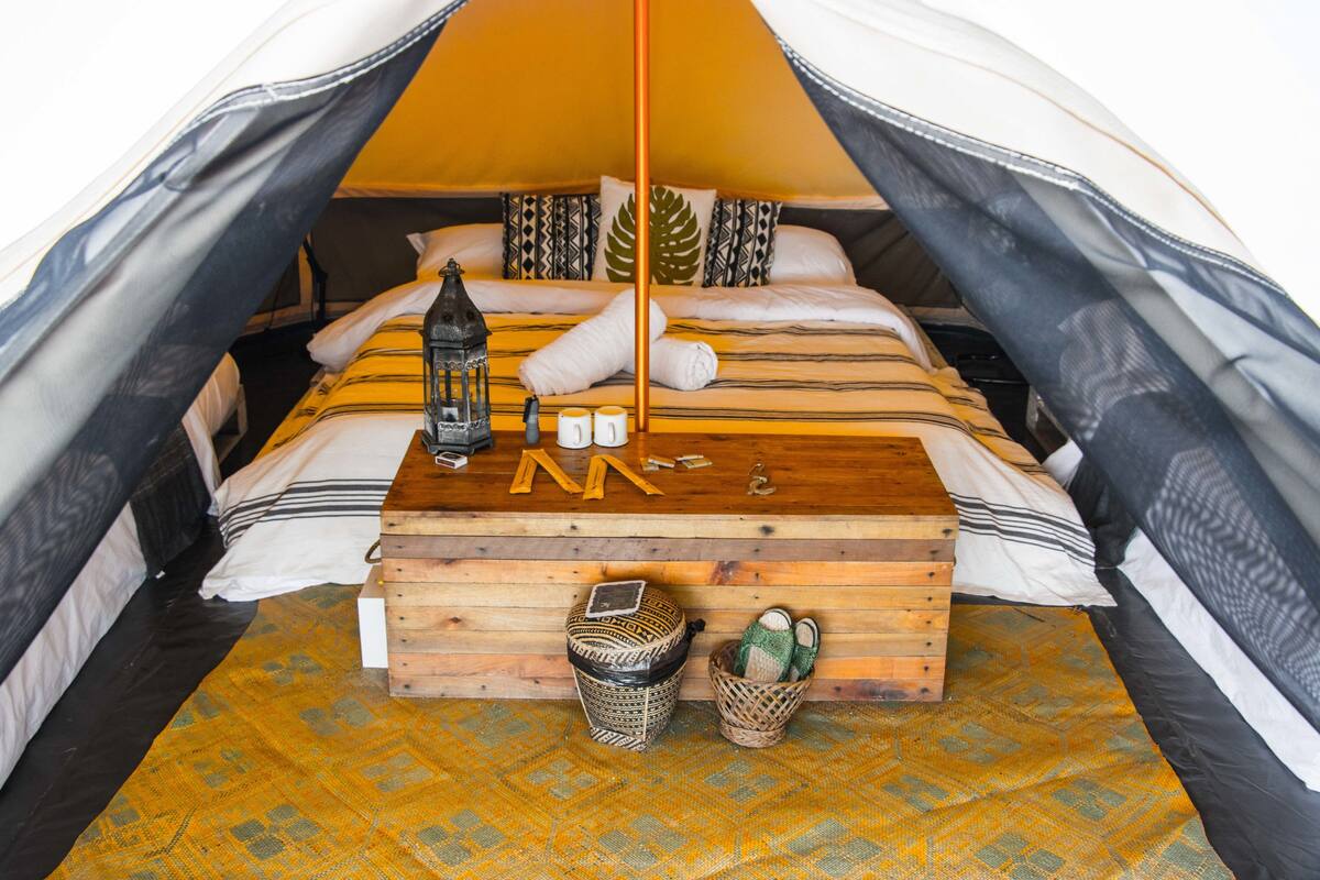 Una tienda acogedora con una cama de madera, un farol y una mesita con una cesta y una caja.