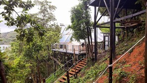 A wooden staircase leading to a wooden deck with a view of a beach and a house in the background. - The Birdhouse El Nido - Glamping (El Nido)