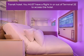 A modern hotel room with a bed, a large mirror, and a wall-mounted TV.