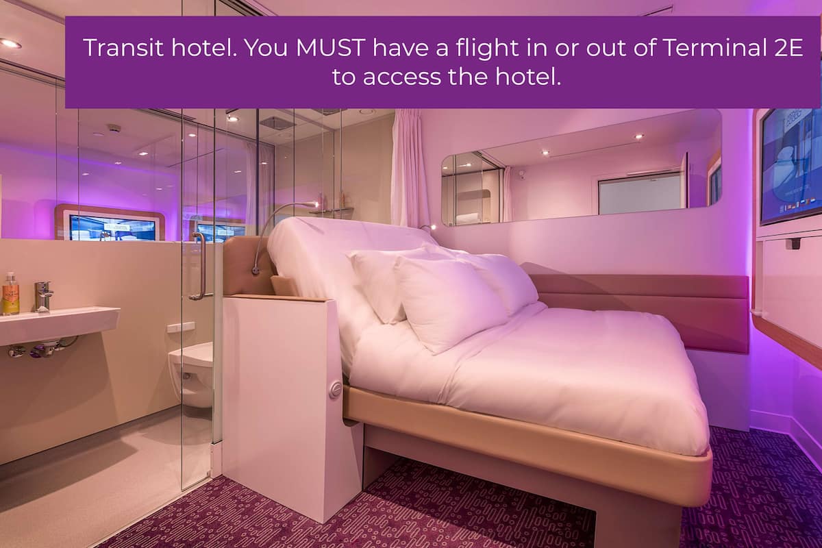 Una habitación de hotel moderna con una cama, una mesita de noche, un espejo y una pantalla de televisión.