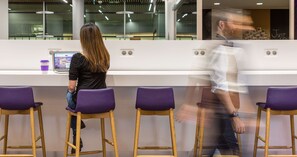 Un interior moderno con una mesa de recepción, taburetes morados y un ordenador portátil sobre la mesa.
