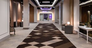 Vestíbulo de hotel con una alfombra de estampado geométrico, un mostrador de recepción y un cartel que dice 'YotelAR'.