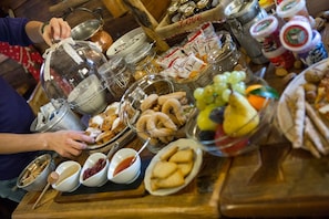 A table with various food items and condiments, including a covered pot, baskets of pastries, and bowls of dips.