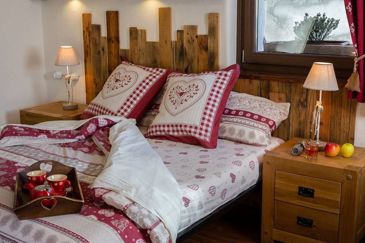 A cozy bedroom with a wooden headboard, checkered pillows, a bedside table with a lamp, and a tray with mugs.