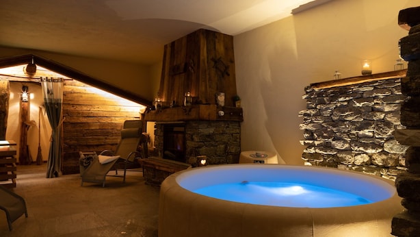 A cozy room with a stone wall, a fireplace, and a hot tub. - La Maison d'Antan (Bionaz)