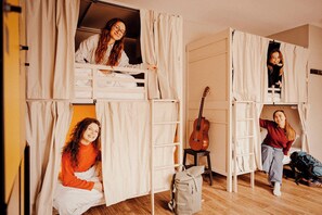 Una habitación tipo dormitorio con literas, una guitarra y una mochila.