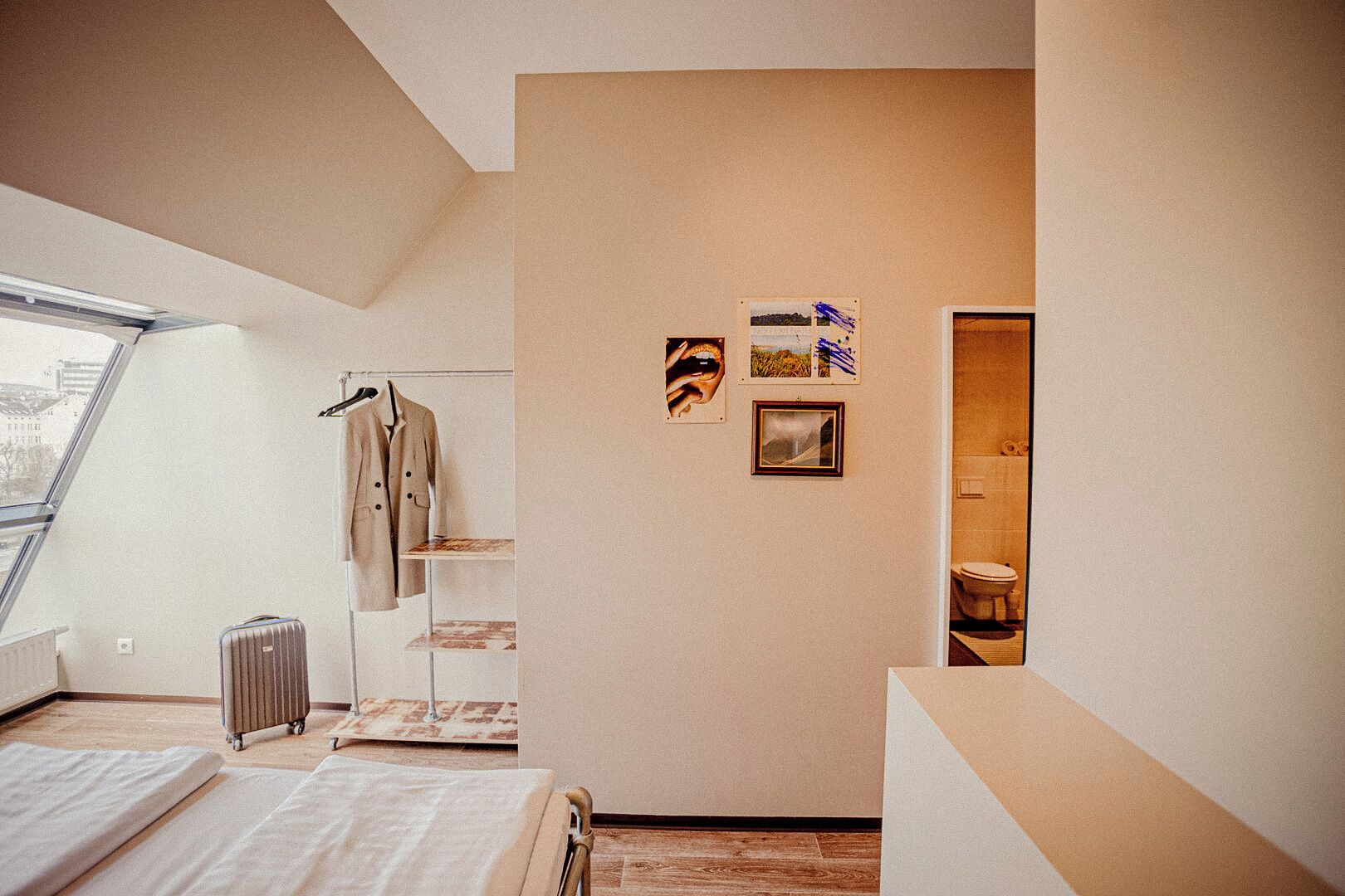 Un dormitorio con cama, un radiador, una maleta, un perchero y una ventana.