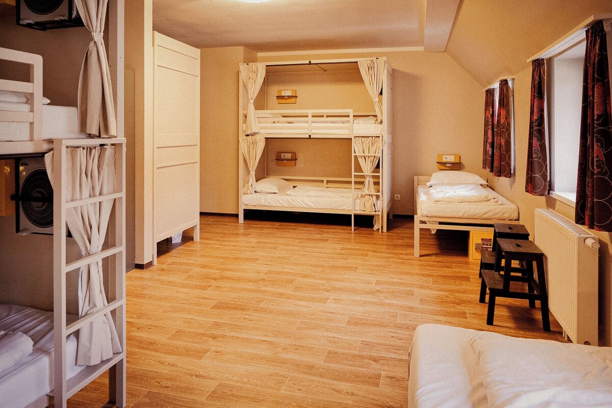 Una habitación con dos literas, suelo de madera, un radiador y una ventana con cortinas.