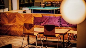 Un intérieur moderne avec un plancher en bois, une table de billard et des coins salon dotés de fauteuils et de coussins.