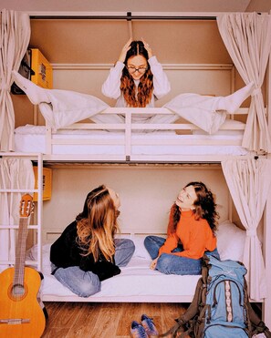 Habitació amb lliteres, una guitarra, una motxilla i una maleta.