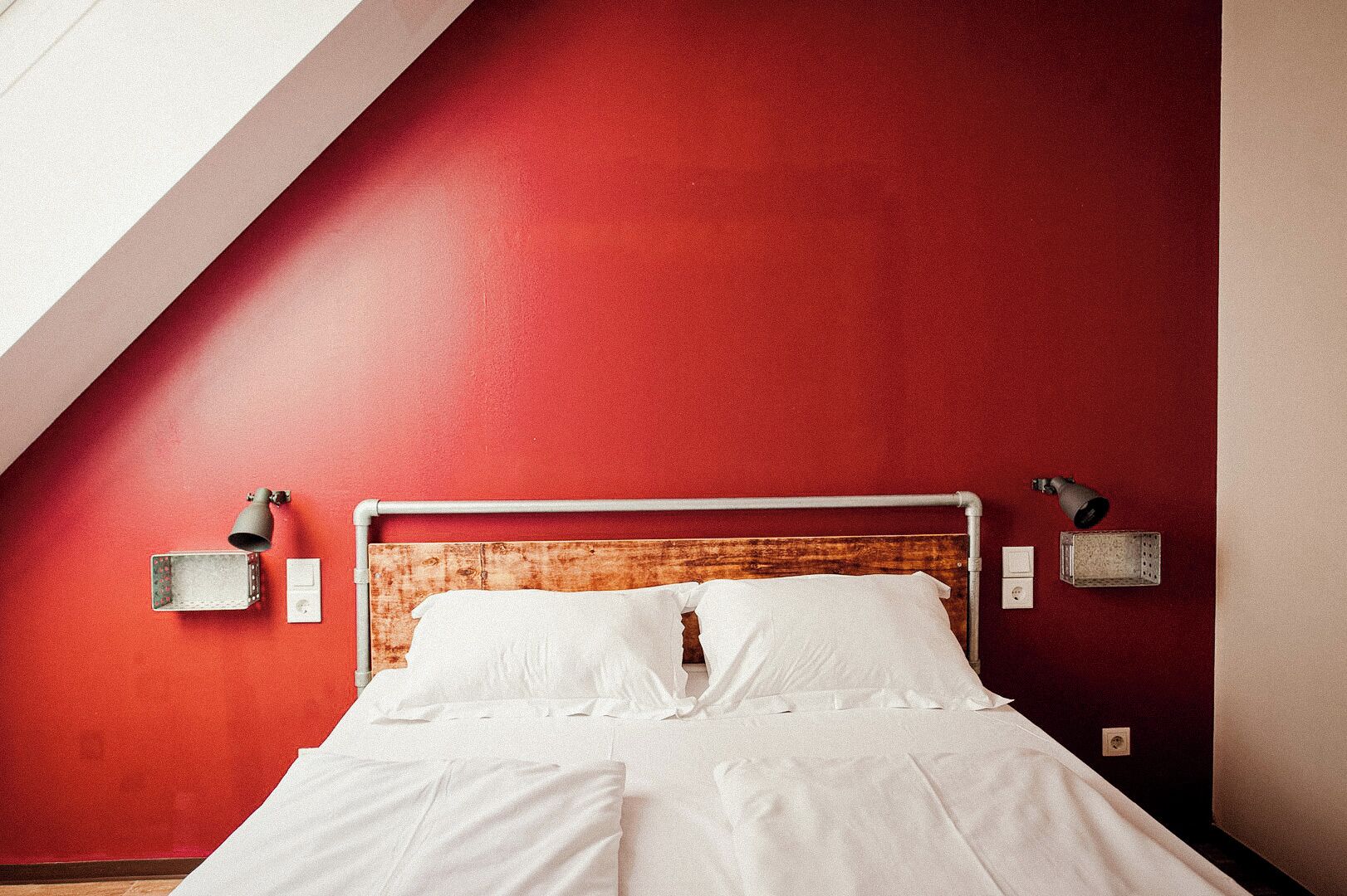 A room with a sloped ceiling, a bed with white bedding, a wooden headboard, and two wall-mounted lamps.