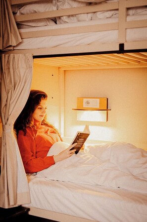 A single bed with a headboard, a bedside table with a lamp, and a wall-mounted shelf with a sign. - Wombat's City Hostel Vienna Naschmarkt (Vienna)