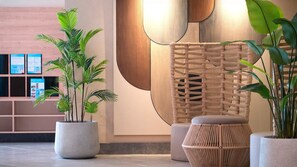 A modern lobby with potted plants, a woven partition, and a seating area.