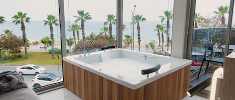Un baño moderno con una bañera independiente, ventanas amplias y vistas al mar y palmeras.