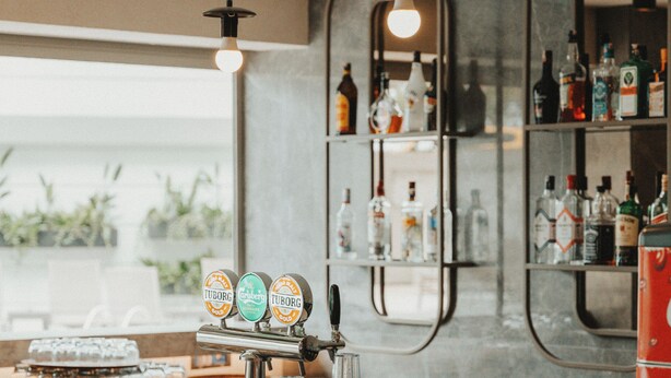 Een bar met een toog, planken met flessen en een hangende lamp.