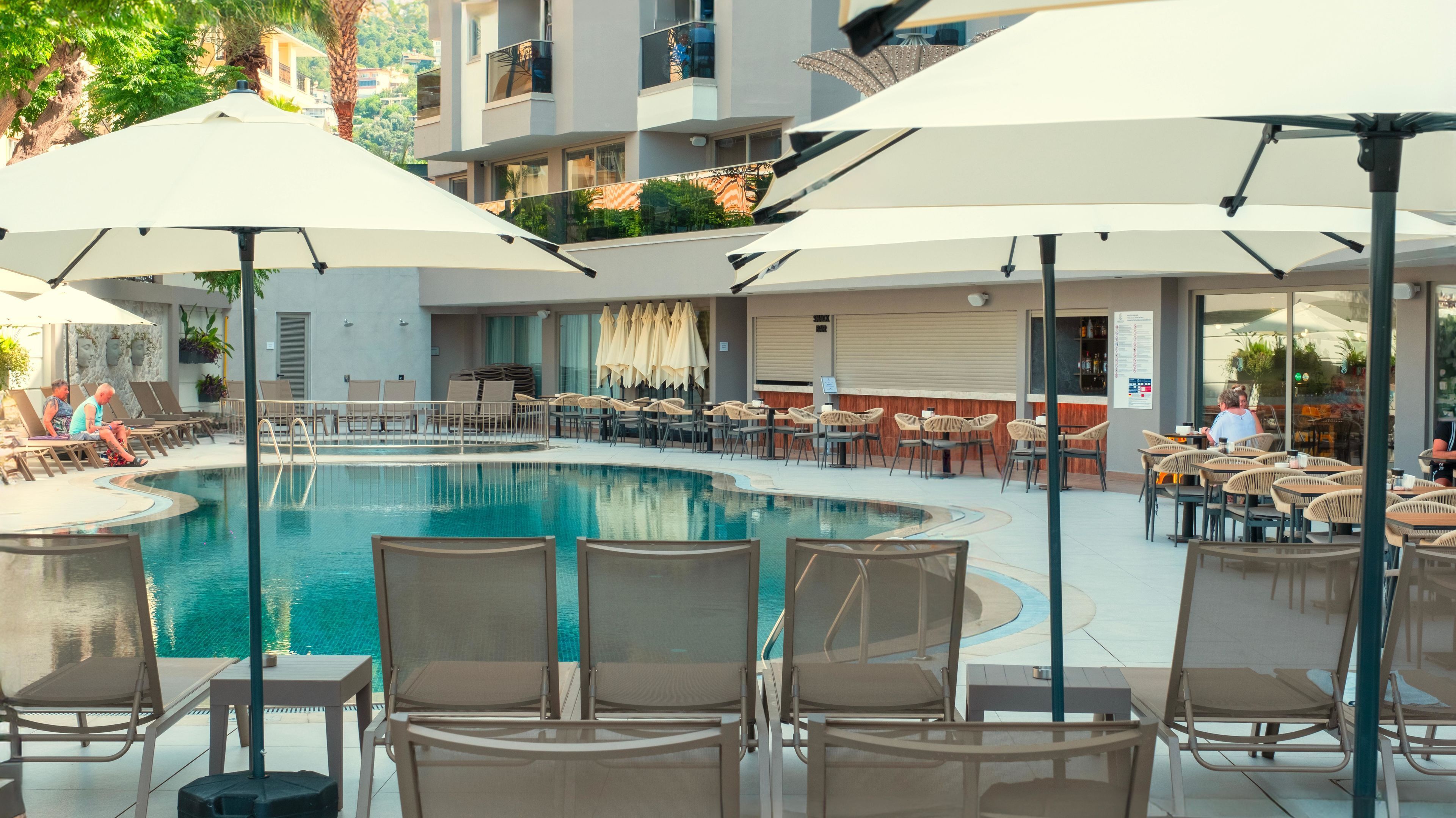 A pool area with lounge chairs and umbrellas, surrounded by a building with multiple floors and balconies.