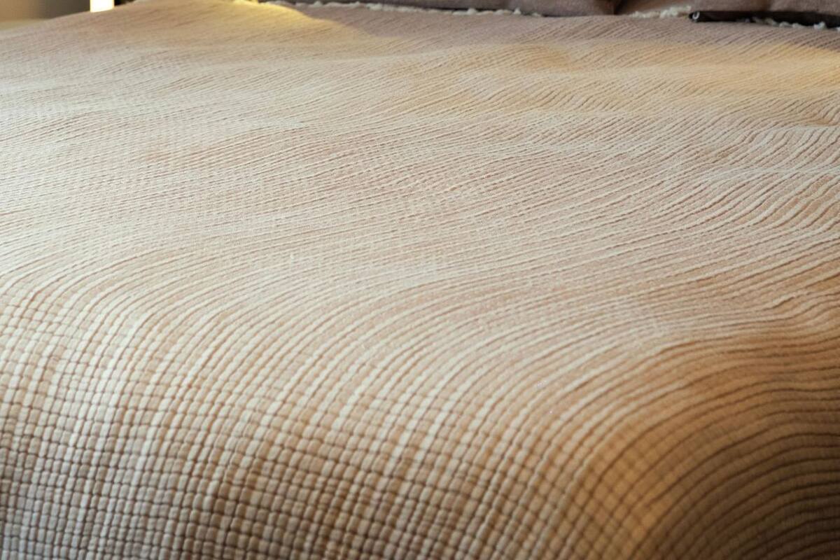 A neatly made bed with a textured beige cover, a grey headboard, and two brown pillows.