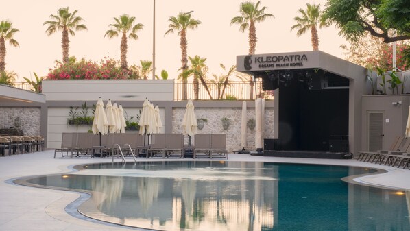 A swimming pool area with lounge chairs and umbrellas, palm trees, and a hotel entrance labeled 'KLEOPATRA DREAMS BEACH HOTEL'.