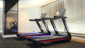 Tre løbebånd i et fitnesscenter med et vindue og en netværkskonstruktion i baggrunden.