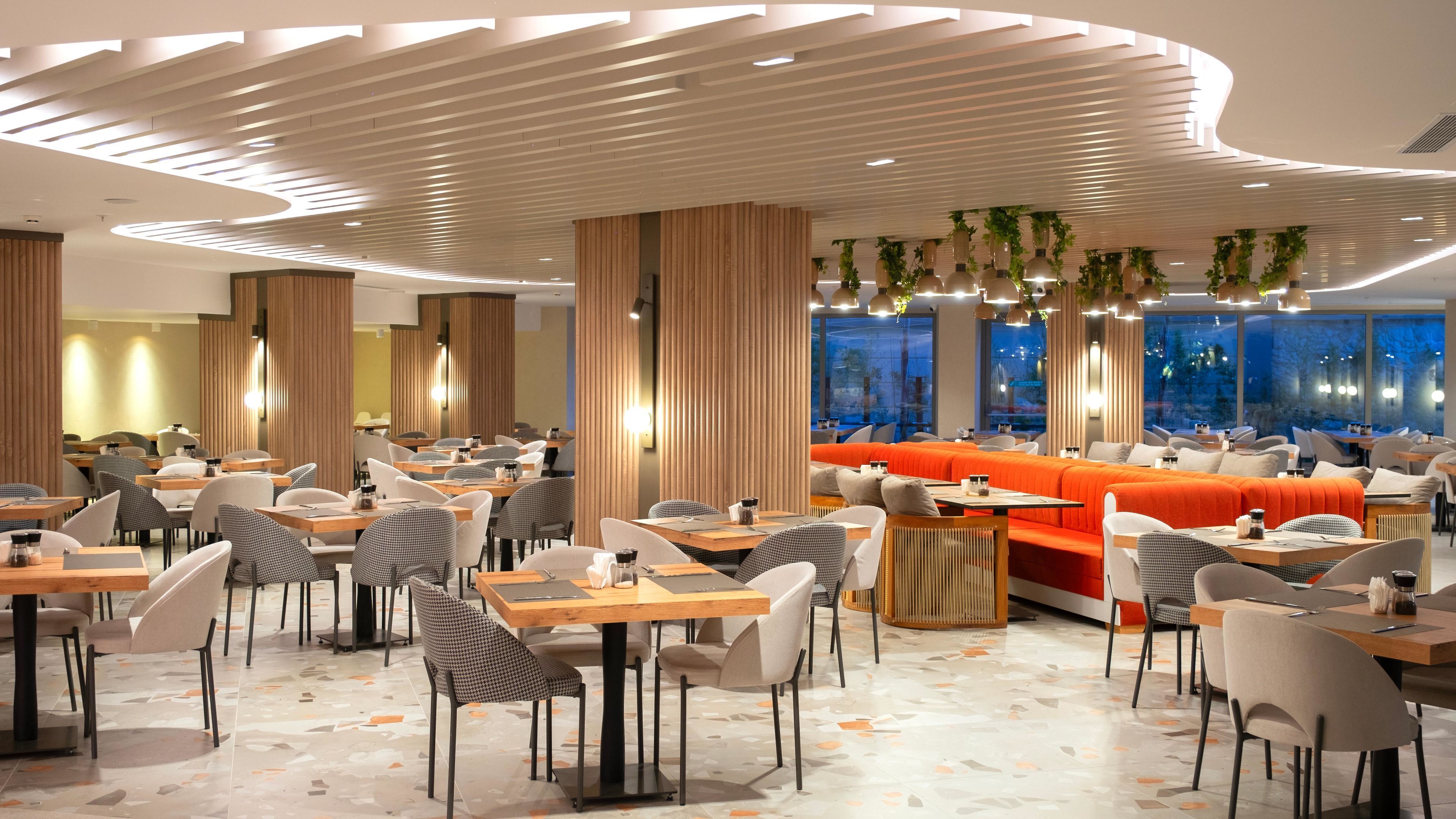 Ein modernes Restaurant mit verschiedenen Sitzgelegenheiten, darunter Tische und eine große, orangefarbene Sofaecke.