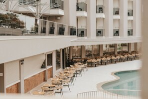 Et moderne hotel med poolområde, flere etager og udendørs siddepladser.