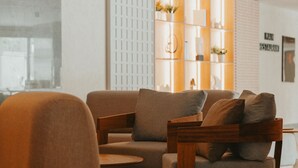 Een moderne zithoek met een bank en fauteuils, een houten salontafel en een decoratieve wandmeubel met planken en planten.