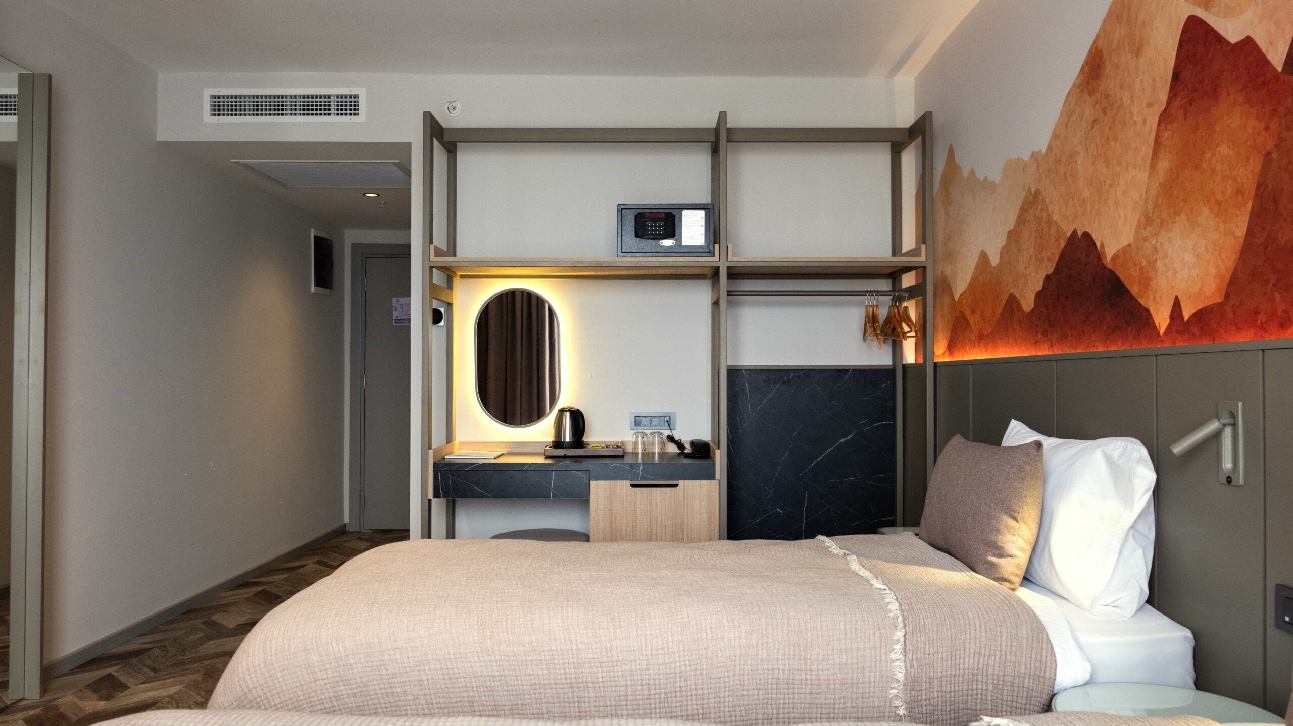 Een hotelkamer met een bed, een bureau met spiegel, een klein kitchenette en een tv aan de muur.