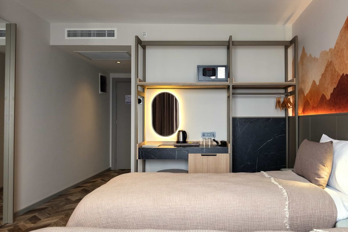 A hotel room with a bed, a desk with a mirror, a small kitchenette, and a wall-mounted TV.