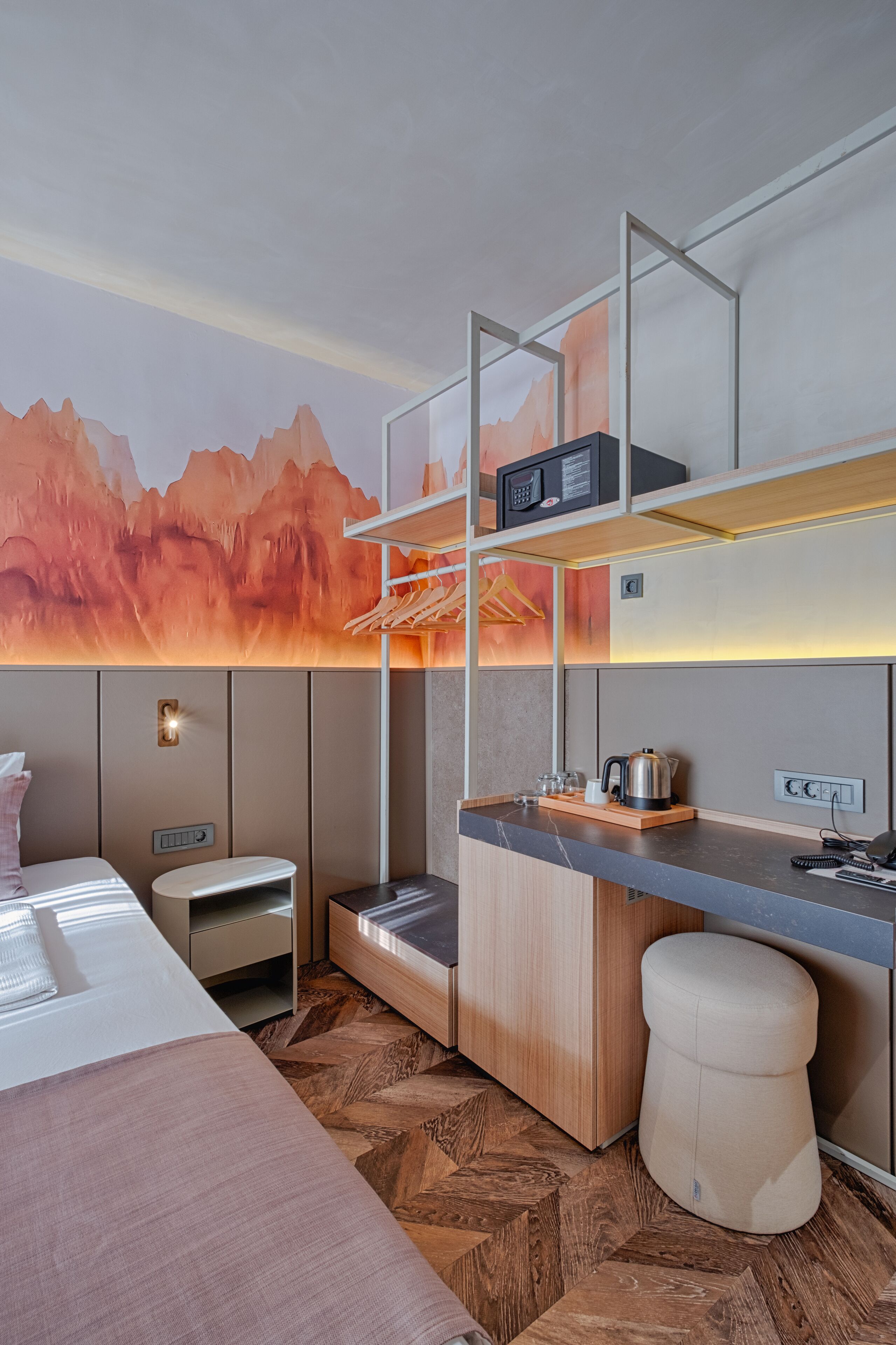 A modern hotel room with a bed, a small desk, a seating area, and a kitchenette.