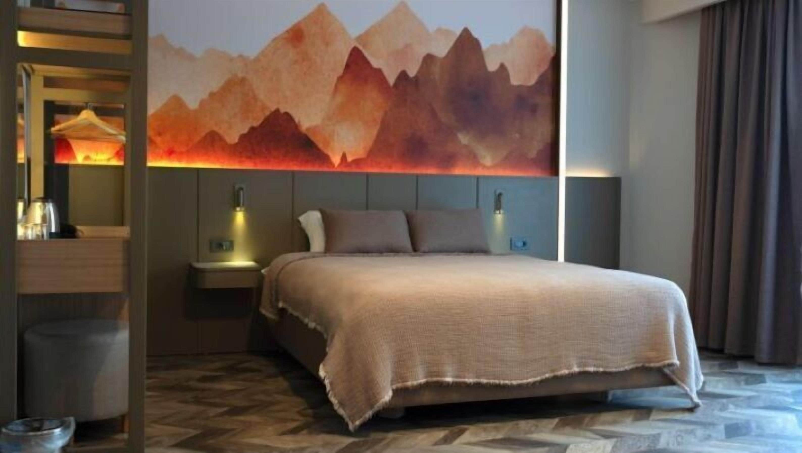 Een hotelkamer met een bed, nachtkastjes, een wandlamp en een groot berglandschap.