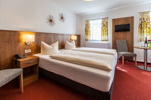 A hotel room with two beds, a desk with a telephone, a chair, a TV mounted on the wall, and a window with curtains. - Sonnebergbaude Waltersdorf (Grossschoenau)