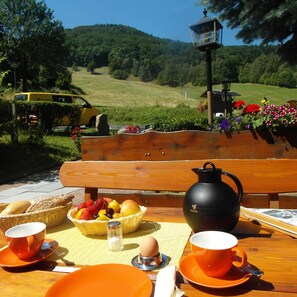 A wooden bench with a table set for breakfast, including bread, fruits, eggs, and cups. - Sonnebergbaude Waltersdorf (Grossschoenau)