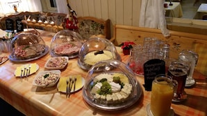 A buffet table with various food items, including meats and cheeses, covered with dome lids. There are also several glasses and a pitcher of juice. - Sonnebergbaude Waltersdorf (Grossschoenau)