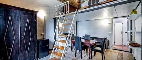 Una habitación con una escalera de madera, un comedor con sillas y una mesa, un armario grande de madera oscura y un techo con diseños ornamentales.