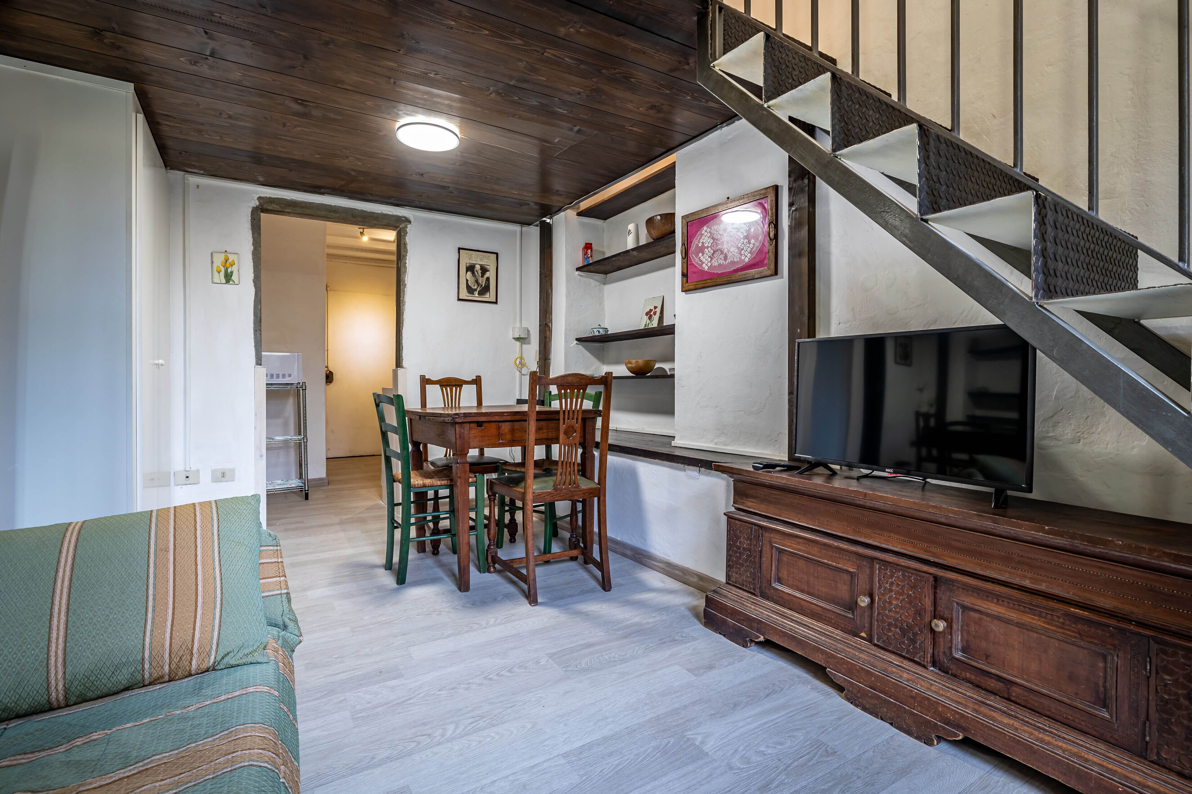 A living room with a wooden staircase, a dining table with chairs, a TV, and a sofa.