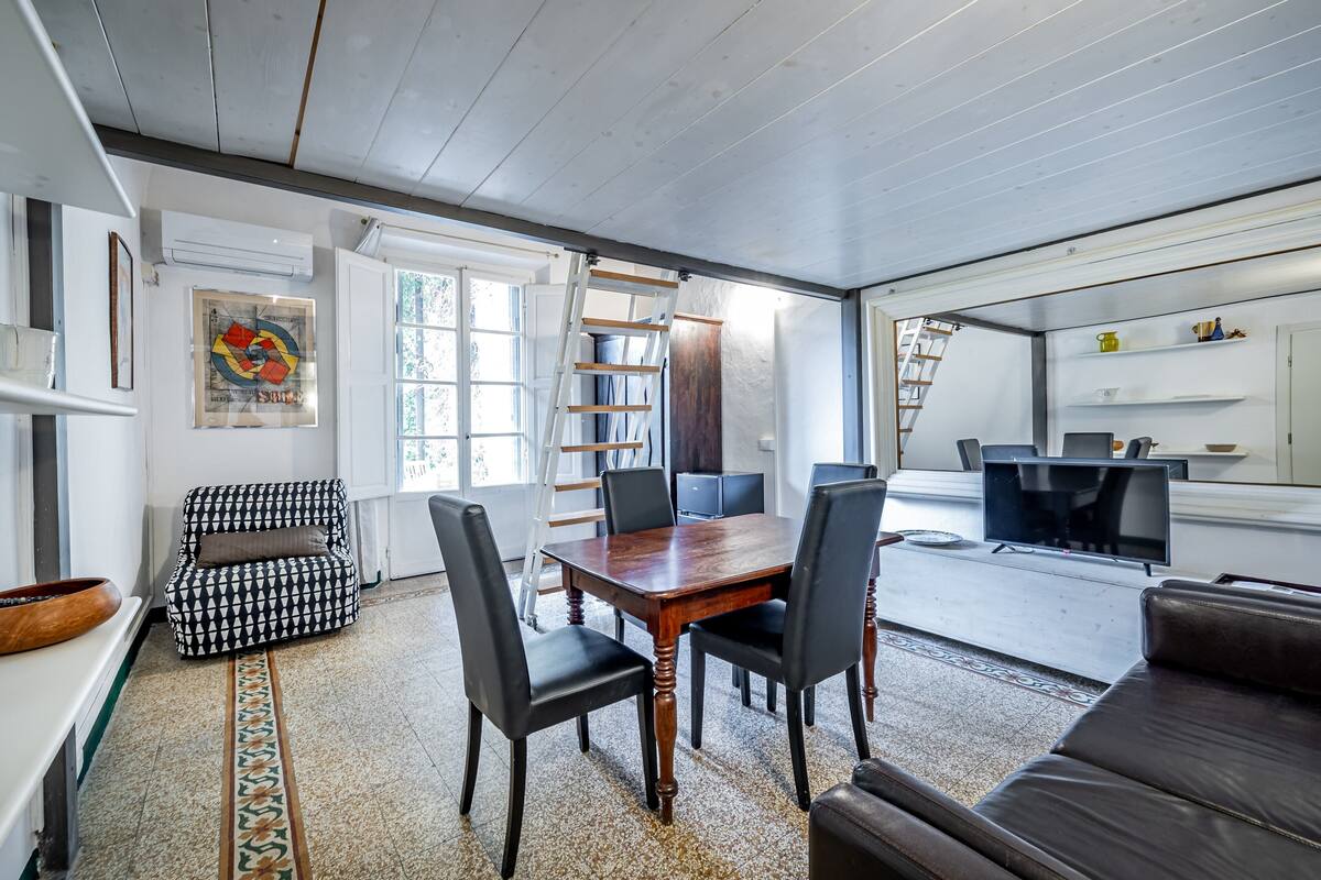A modern living room with a wooden dining table, black leather chairs, a patterned rug, and a black leather sofa.