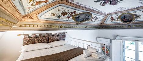 A hotel room with a large bed, a ceiling with ornate designs, and a window with a view.