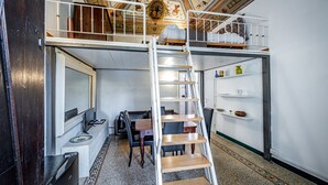 Een kleine kamer met een stapelbed, een bureau en een stoel. Een ladder verbindt de twee niveaus.