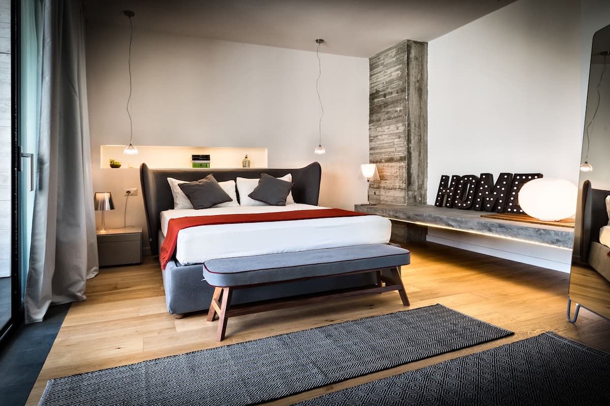 Un dormitorio moderno con cama, banqueta, mesitas de noche y estante en la pared.