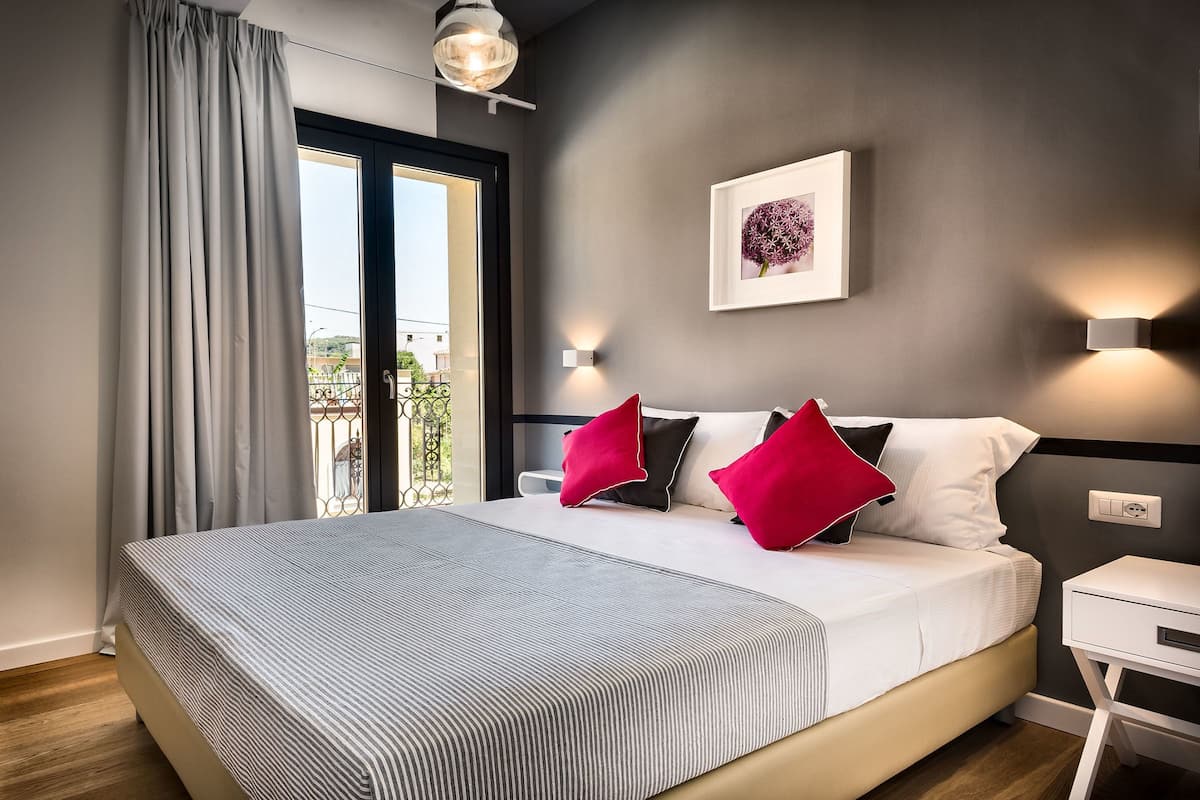Una habitación de hotel moderna con una cama grande, vistas a través de una puerta corredera, una obra de arte enmarcada en la pared y una mesita de noche.