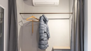A compact room with a wooden floor, a coat rack with a jacket, a small shelf, and a wall-mounted air conditioner. - Flospirit - San Lorenzo (Florence)