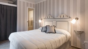 A neatly made bed with a headboard, two bedside lamps, and a door leading to a bathroom. - Flospirit - San Lorenzo (Florence)