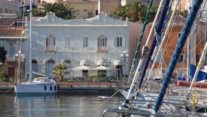 A marina with boats docked, a building with balconies, and a clear sky. - Hotel Hieracon (Carloforte)